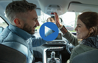 Man and woman in car giving high five with play button