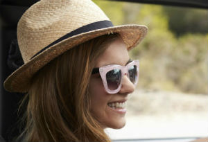 A woman wearing sunglasses and a sun hat driving a car